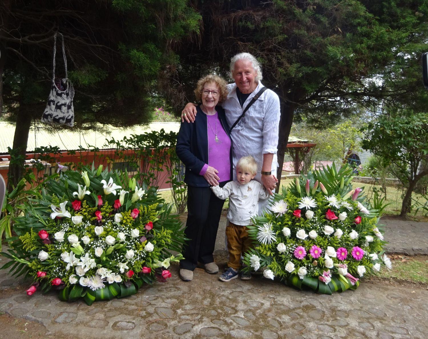 Denise Rauber und Omrael Norbert Muigg mit einem kleinen Kind zwischen zwei großen Blumengestecken